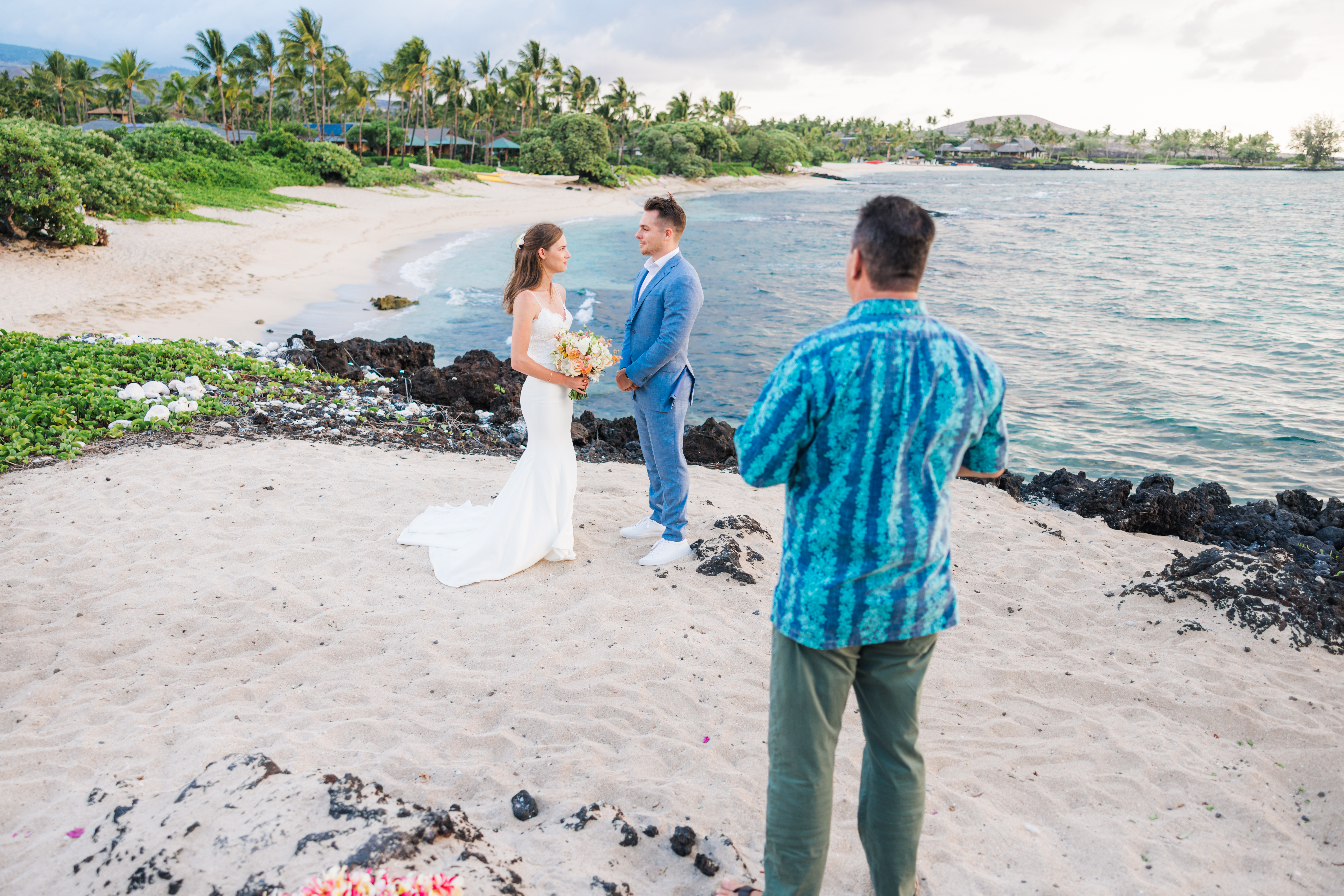Couple on a lava cliff overlooking a gorgeous beach during this Big Island elopement.