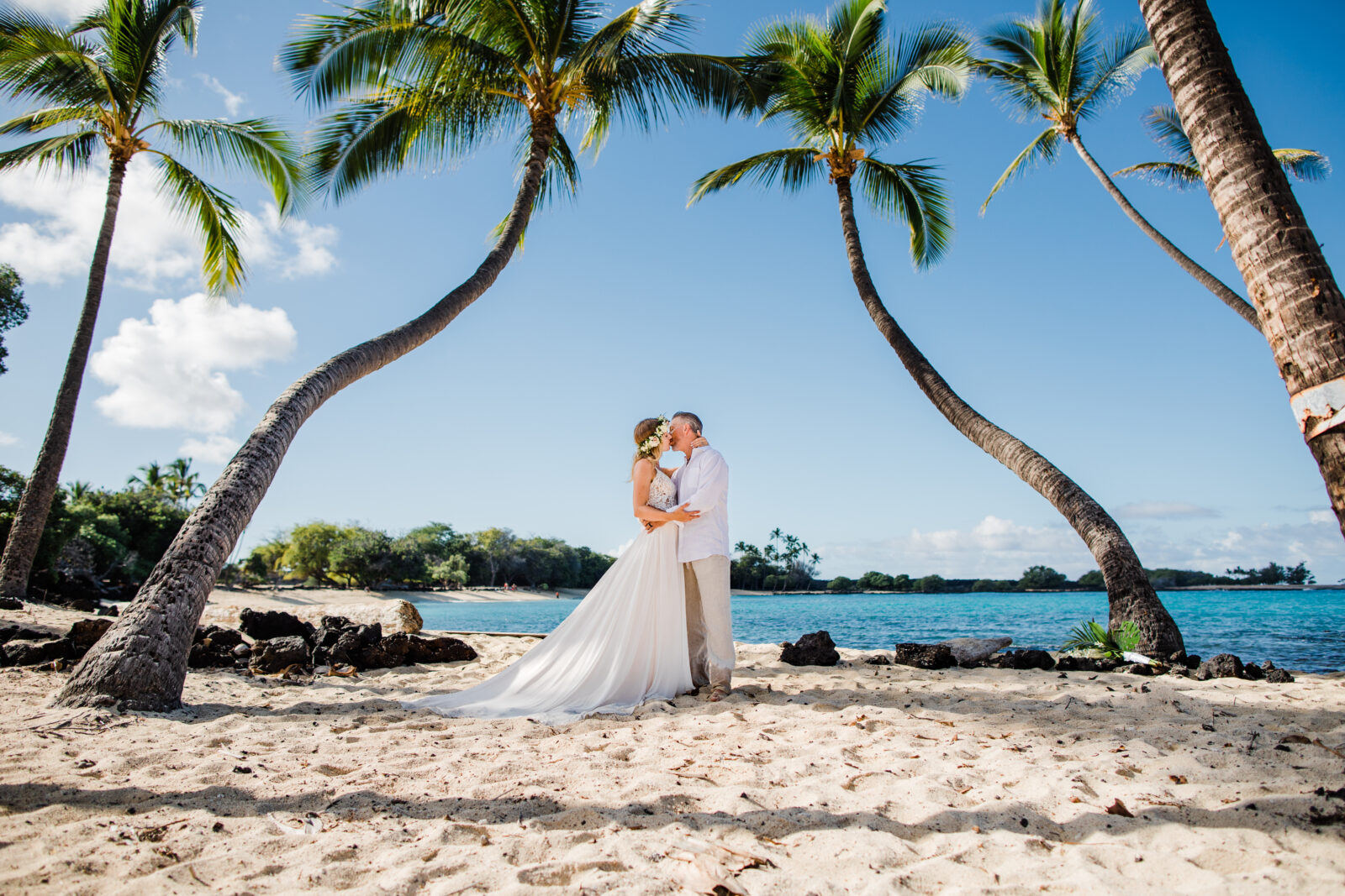 Between the palms, a couple on a secluded beach after their Big Island elopement.